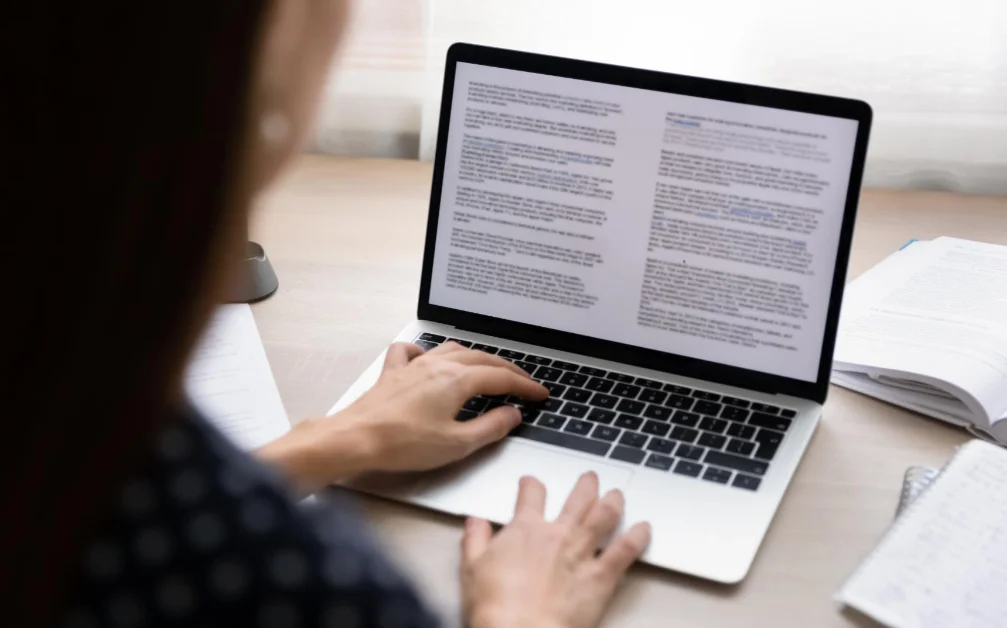 a woman is using a laptop with a book on it.