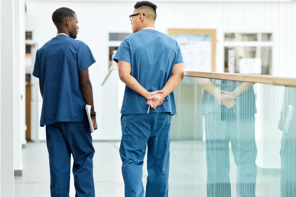 two men in blue scrubs walking down a hallway.